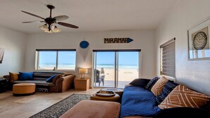 A spacious living room with a large window overlooking a beach, a ceiling fan, and a sign that reads "MIRAMAR". - Fully Remodeled, The Suite at Rocky Point 2 Ocean front (Puerto Penasco)