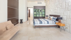 A modern bedroom with a large bed, a sofa, and a green shelving unit.