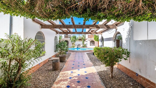 Un patio con piscina, rodeado de muros blancos y pérgolas de madera.