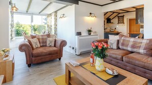 A spacious living area with a brown leather sofa, a wooden coffee table, and a view into the kitchen. - Serenity Sands - UK30265 (Goodrington, near Paignton)