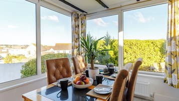 A dining area with a table, chairs, a potted plant, and a view of the outside.