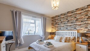 A bedroom with a bed, bedside tables, a TV, and a wall with a wooden plank design. - Serenity Sands - UK30265 (Goodrington, near Paignton)