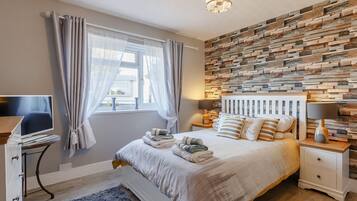 A bedroom with a bed, bedside tables, a TV, and a wall with a wooden plank design.