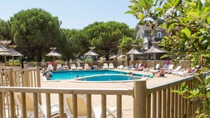 A pool area with lounge chairs and umbrellas, surrounded by wooden fencing and trees. - Appart Duplex à Lac Hourtin | Accès Piscine (Hourtin)