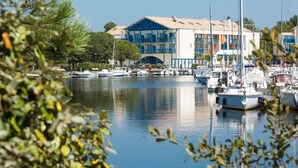 A marina with boats docked, a building with balconies, and a clear sky. - Appart Duplex à Lac Hourtin | Accès Piscine (Hourtin)