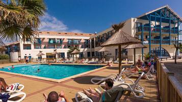 Relax by the pool surrounded by lounge chairs and umbrellas, with a thatched roof nearby.
