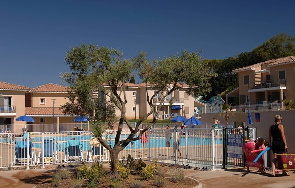 Zona de piscina con piscina cercada, sillas de descanso y sombrillas.