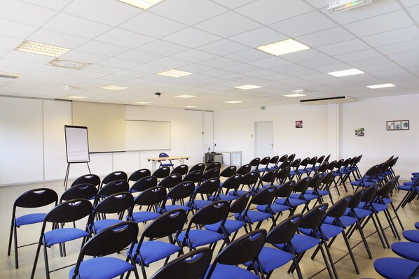 Un salón de conferencias con filas de sillas, una pizarra y un proyector.
