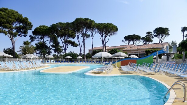 Ein Swimmingpool mit blauen und weißen Liegestühlen, einer Rutsche und Bäumen im Hintergrund.