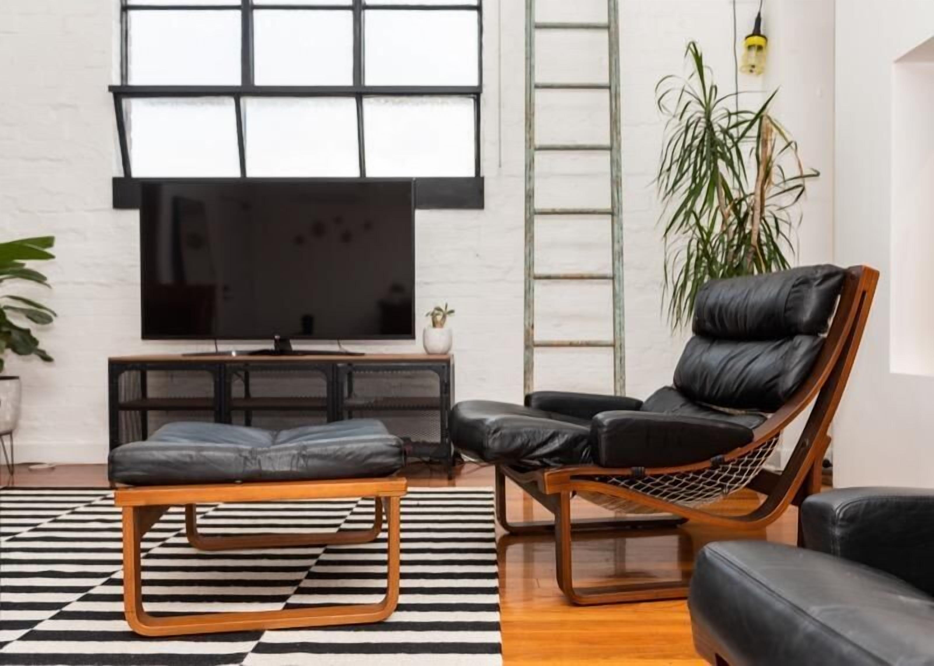 Una sala de estar moderna con un televisor de pantalla plana grande, un sofá de cuero negro, una mesa de centro de madera y una alfombra a rayas blanco y negro.