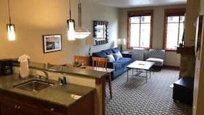 A compact living space with a kitchen area, dining table, sofa, and a patterned carpet.
