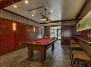 Enjoy a game of pool in this spacious room with a pool table, surrounded by comfortable seating and a large window offering a view.