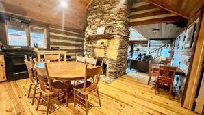 A rustic cabin interior with a stone fireplace, wooden dining table, and chairs. - Authentic Log Cabin on Dancy Mountain near McGrady, North Carolina (McGrady)
