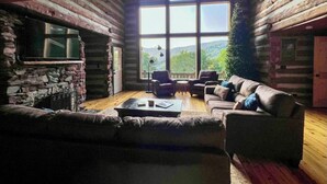 A log cabin interior with a stone fireplace, a large window offering a view of the outdoors, and a cozy seating area with a sofa and armchairs. - Authentic Log Cabin on Dancy Mountain near McGrady, North Carolina (McGrady)