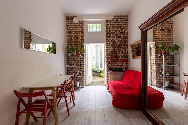 A room with a brick wall, a red sofa, a dining table with chairs, and a guitar leaning against the wall.