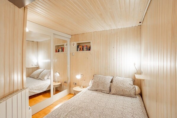 A bedroom with a bed, bedside tables, a mirror, and built-in bookshelves.
