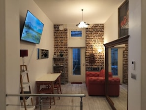 Una sala de estar moderna con un sofá rojo, un televisor montado en la pared, una chimenea y una zona de cocina con una pared de ladrillo.