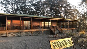 A wooden cabin with a balcony, a gravel driveway, and a bench. - Bela Vista Spa Cabin (Vacy)
