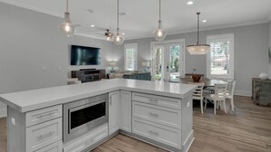 Une cuisine moderne dotée d’un grand îlot central, d’appareils électroménagers intégrés et de luminaires suspendus.
