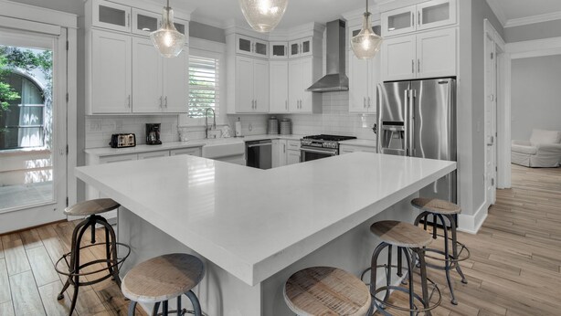 Une cuisine moderne avec des meubles blancs, un grand îlot central doté de tabourets, des appareils en acier inoxydable et un éclairage suspendu.