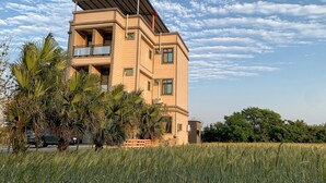 A modern multi-story building with balconies, surrounded by palm trees and a field. - White Cat B&B (Jinning)