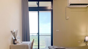 A hotel room with a bed, a table with a chair, a window with a view of greenery, and an air conditioning unit. - White Cat B&B (Jinning)