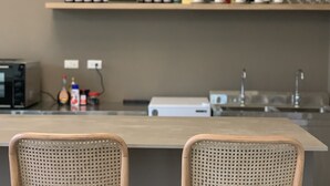 A kitchen with a bar area, featuring a wooden table and two wicker chairs. There are wine bottles and glasses on a shelf above the counter. - White Cat B&B (Jinning)