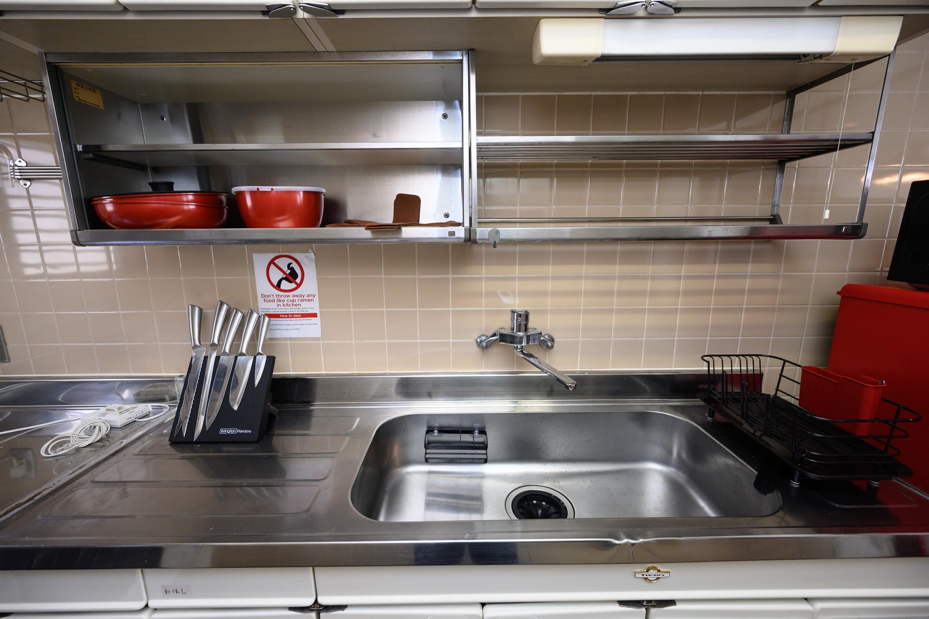 A stainless steel kitchen sink with a dish rack, a knife block, and a red container on the counter.