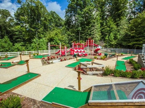 Un parcours de mini-golf doté d’une structure de jeu rouge et blanche, entouré d’une clôture blanche et d’une végétation luxuriante.