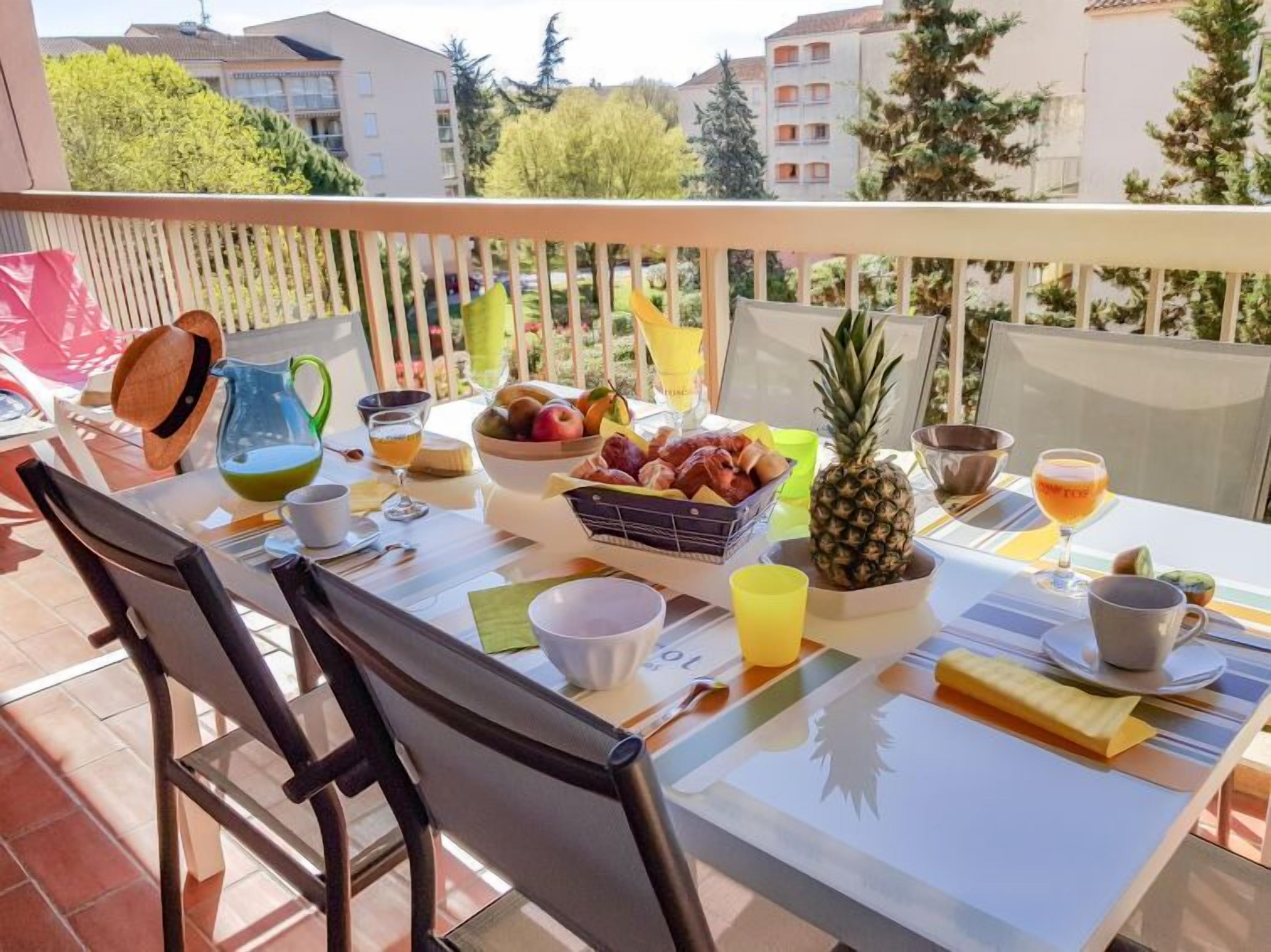 Ein Balkon mit Tisch, gedeckt für ein Frühstück, inklusive Früchte, einer Ananas und Getränke.
