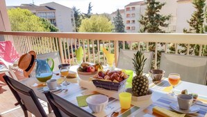 Un balcón con una mesa dispuesta para el desayuno, que incluye frutas, una piña y bebidas.