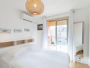A bedroom with a large bed, a ceiling fan, a window with curtains, and a view of the outside.