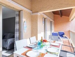 A dining area with a table set for two, a bed with a canopy, and a view of the sea through a glass door.