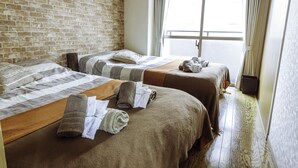 A hotel room with two beds, a brick wall, a large window with curtains, and a wooden floor. - Nestle Tokyo Deluxe Akihabara 05 (Tokyo)
