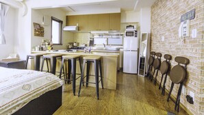 A compact kitchen with wooden cabinets, a central island with stools, a refrigerator, and a microwave. - Nestle Tokyo Deluxe Akihabara 05 (Tokyo)