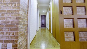 A narrow hallway with a wooden floor, brick walls, and a door with a window design. - Nestle Tokyo Deluxe Akihabara 05 (Tokyo)