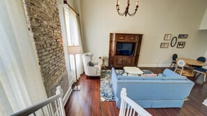 A living room with a blue sofa, wooden flooring, a chandelier, and a stone wall.