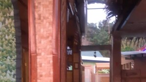 Um corredor estreito com paredes de tijolo e grades de madeira, que leva a uma área coberta com telhado.