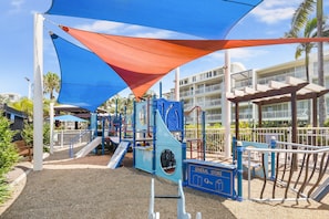 Children can play safely on the rubberized ground beneath the shaded play area with climbing structures and slides.