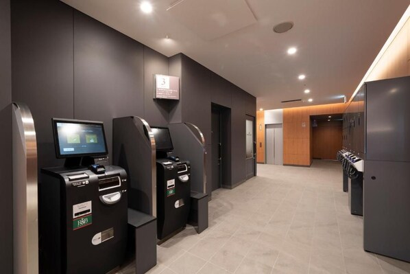 Un área de ascensores moderna con pantallas digitales y lectores de tarjetas, un cartel que indica el piso y un lavadero con electrodomésticos de estilo industrial.