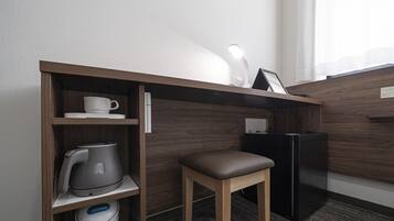 Habitación de hotel compacta con kitchenette, un pequeño escritorio con silla, refrigerador y cafetera.