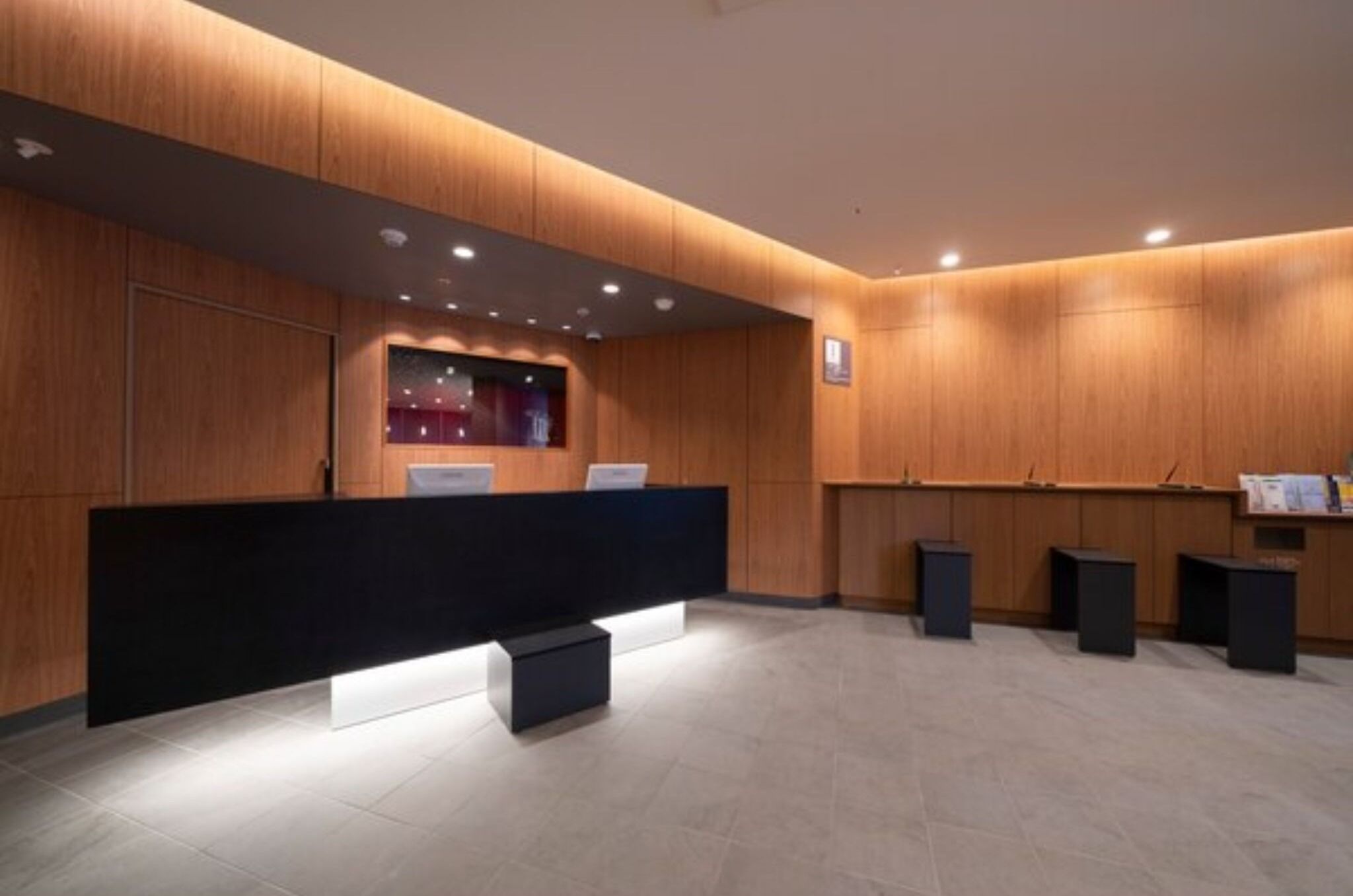 Una moderna área de recepción con un mostrador negro, paneles de madera y luces empotradas.