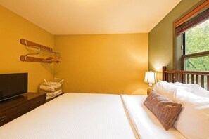 Une chambre d’hôtel avec un lit, une télévision, une lampe et une fenêtre donnant sur des arbres.