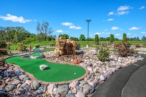 Een midgetgolfbaan met een groen puttingoppervlak, een rotsformatie als hindernis en een houten hek op de achtergrond.
