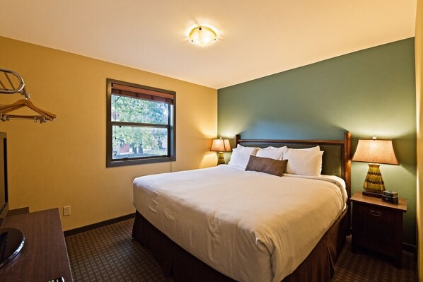 A hotel room with a bed, bedside lamps, a window, and a coat rack.
