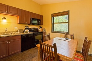 Une cuisine avec des meubles de rangement en bois, un four à micro-ondes, une cuisinière et une table à manger avec des chaises.