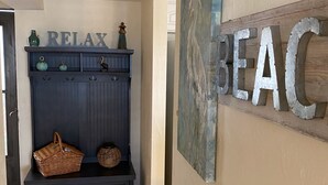 A hallway with a dark blue bench, a basket, and a wall with 'RELAX' and 'BEAC' signs. - Ground floor newly remodeled large condo on car free section-New Smyrna Beach  (New Smyrna Beach)