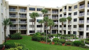 A multi-story hotel with balconies, a well-maintained lawn, and palm trees. - Ground floor newly remodeled large condo on car free section-New Smyrna Beach  (New Smyrna Beach)