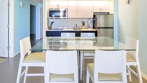 Una cocina moderna con armarios blancos, una mesa de comedor de vidrio y sillas blancas.