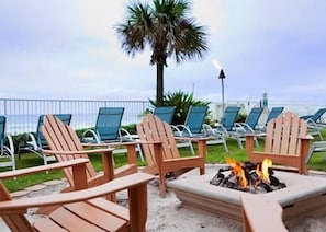 Un área de descanso junto a la playa con sillas Adirondack y una fogata.